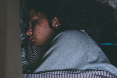Eine junge ME/CFS-Betroffene mit lockigen schwarzen Haaren liegt erschöpft im Bett.